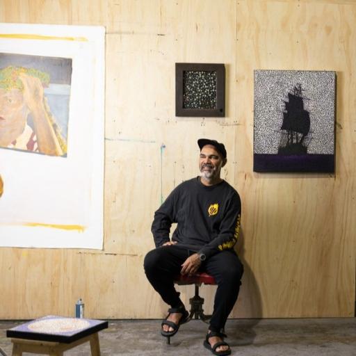 Daniel Boyd sitting in front of his artworks in his Marrickville studio