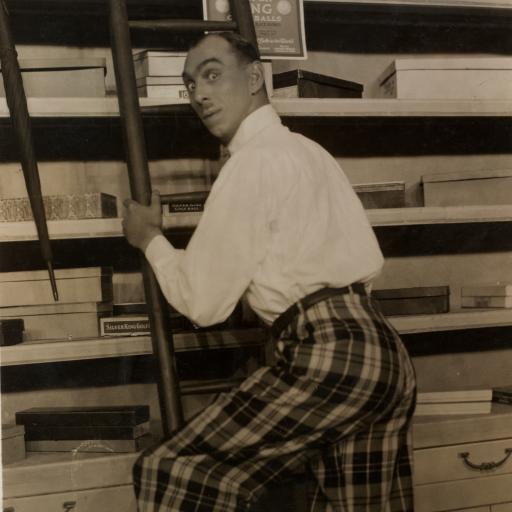 A man in a storeroom climbing a ladder and looking over his shoulder.